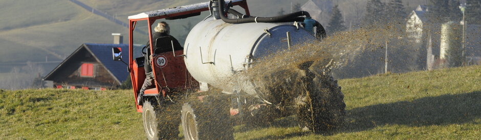 Auf einer Bergeweide. Im Vordergrund fährt ein Bauer mit dem Transportfass und bringt die Gülle aus
