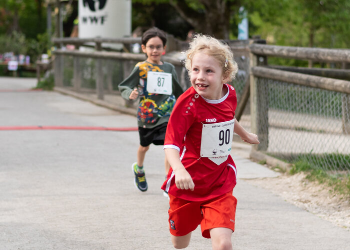 Ein rennendes, lächelndes Kind, in roter Sportbekleidung, welches an einem Lauf im Walter Zoo teilnimmt.