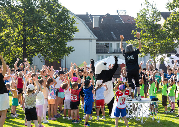 Die teilnehmenden Kinder des WWF-Lauf machen beim Einturnen mit und schauen zum Panda und der Einturner:in auf dem Podest.