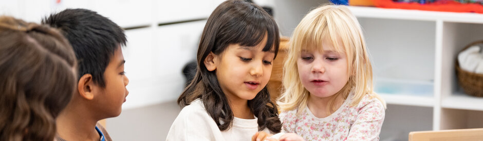 Vier Kinder bestaunen ein Objekt, das für uns nicht erkennbar ist, welches eines der Mädchen in den Händen hält.