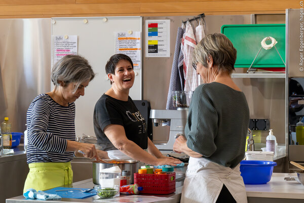 Zwei Kursteilnehmerinnen und die Kursleiterin Anita stehen, lachen und arbeiten in der Schulküche des landwirtschaftlichen Zentrums Salez.