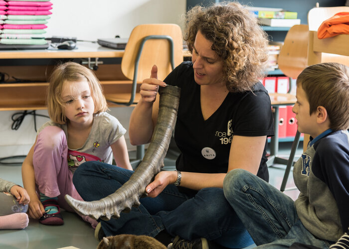 Eine WWF-Schulbesucherin zeigt ein Horn von einem Steinbock zwei Schulkindern