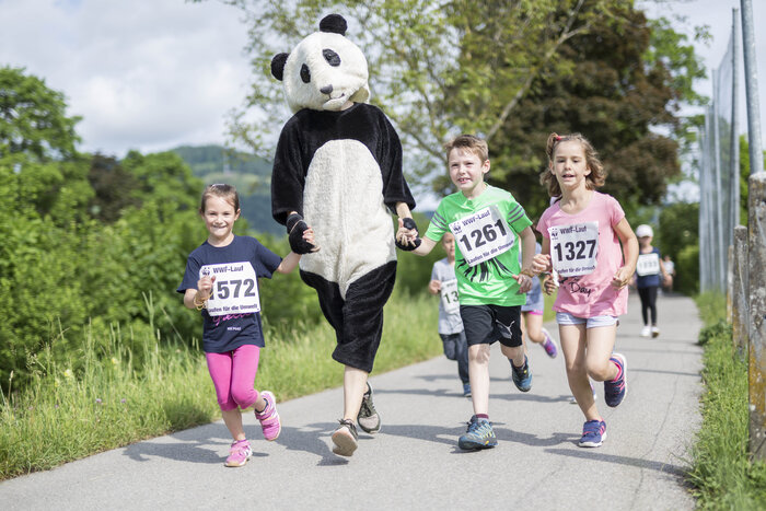 Der WWF-Panda läuft gemeinsam mit drei Kindern einen Kiesweg entlang. 