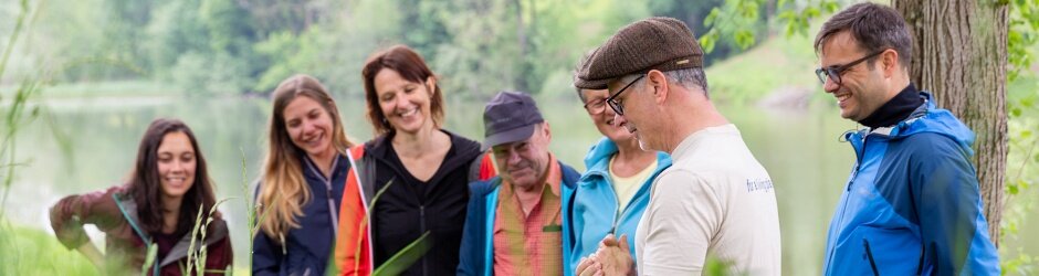Eine Gruppe von freiwilligen Helfern steht an einem Weier. Die Menschen lauschen lächelnd den Instruktionen des Eventleiters.