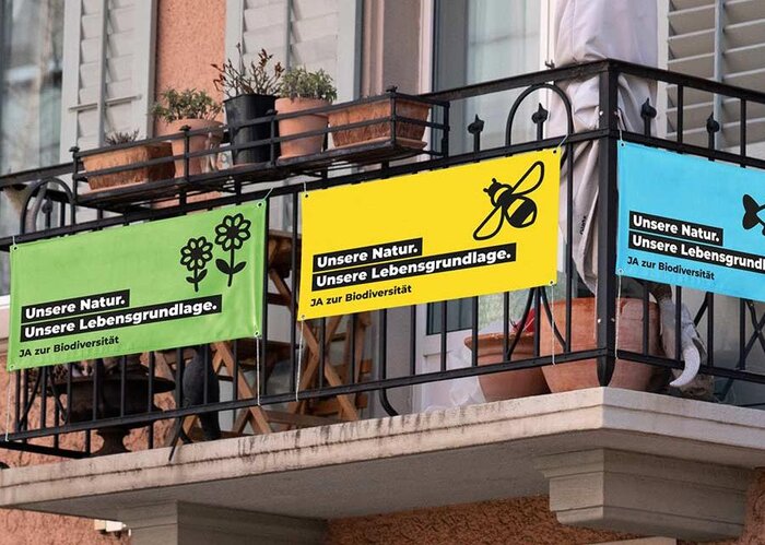 Drei Abstimmungsfahnen hängen an einem Balkon und werben für ein Ja zur Biodiversitätsinitative mit der Abstimmung vom 22. September 2024